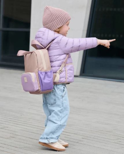 small girl in a puffer jacket and pink beanie and jeans pointing with a 7m backpack
