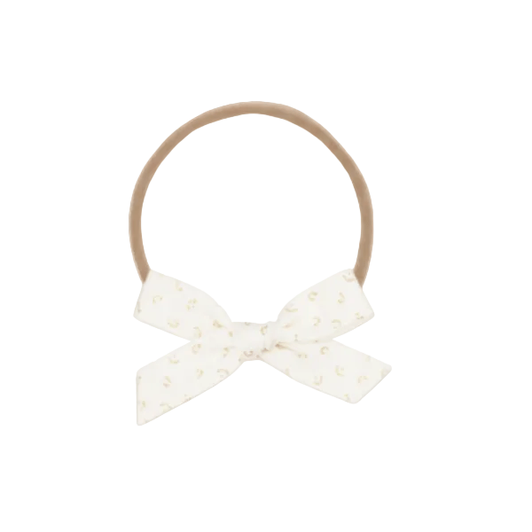 A tan elastic hair tie with a white fabric bow printed with small gold crescent moons, displayed against a textured cream background.