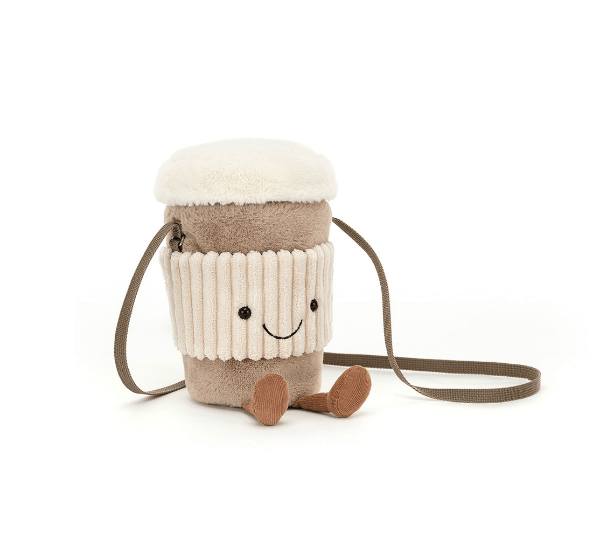 A plush coffee cup crossbody bag with a cream-colored faux-fur foam top, a cream ribbed sleeve, and a brown body, featuring a smiling face and small brown legs. It has a brown shoulder strap on a clean white background.