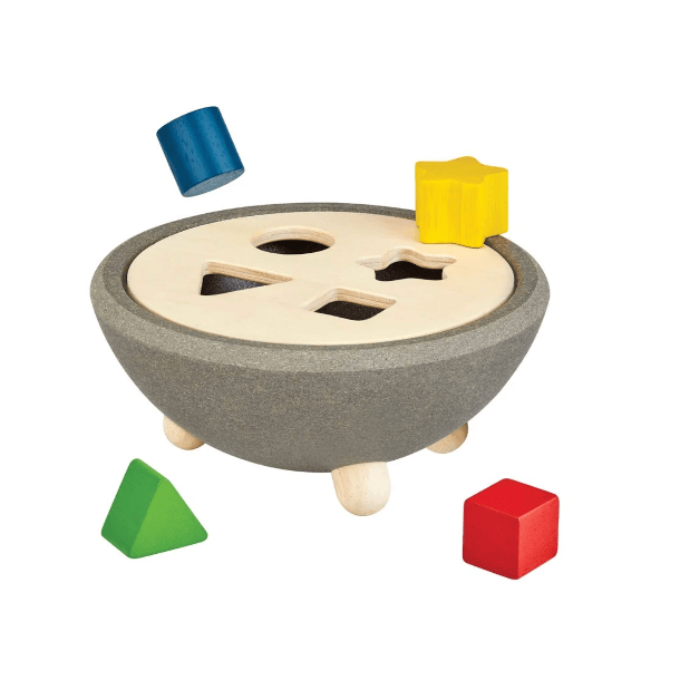 A wooden shape-sorting toy set on a white background, featuring a gray and beige bowl-shaped base with four holes, surrounded by colorful wooden blocks in blue, yellow, green, and red.