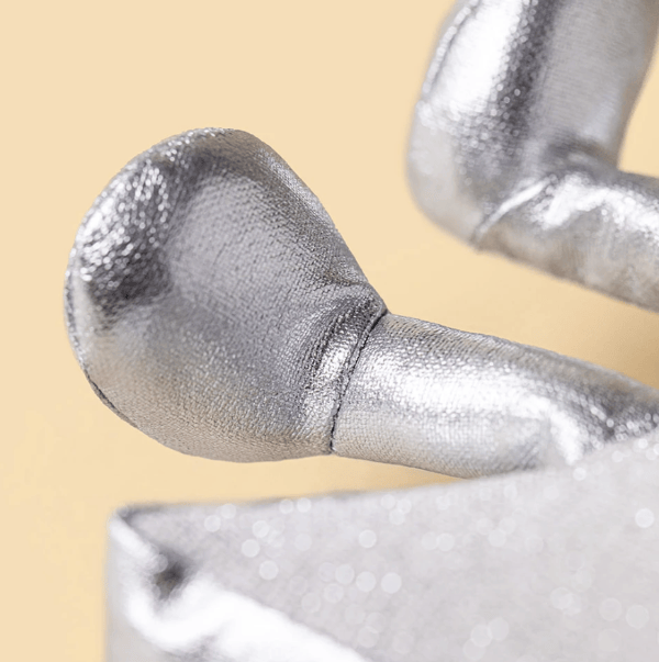 Close-up of a metallic silver textured object with a rounded bulbous end and curved arm, set against a soft warm beige background.