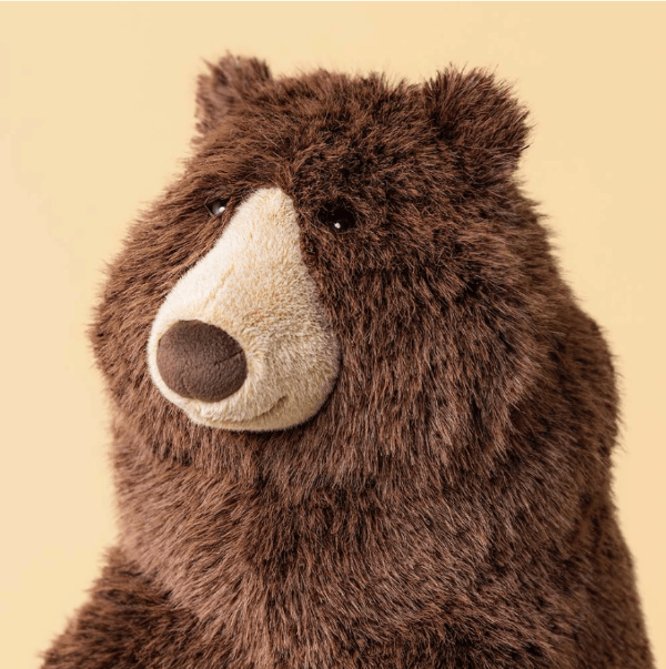 A close-up of a brown plush bear toy with a cream-colored snout and nose, photographed against a solid pale yellow background.