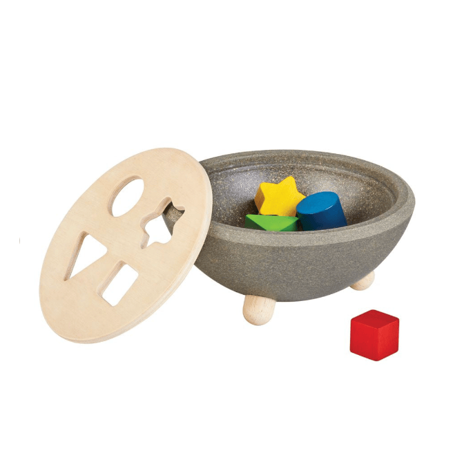 A wooden toy puzzle bowl set with a speckled gray bowl and lid, colorful geometric shapes inside, and a loose red cube on a white background.