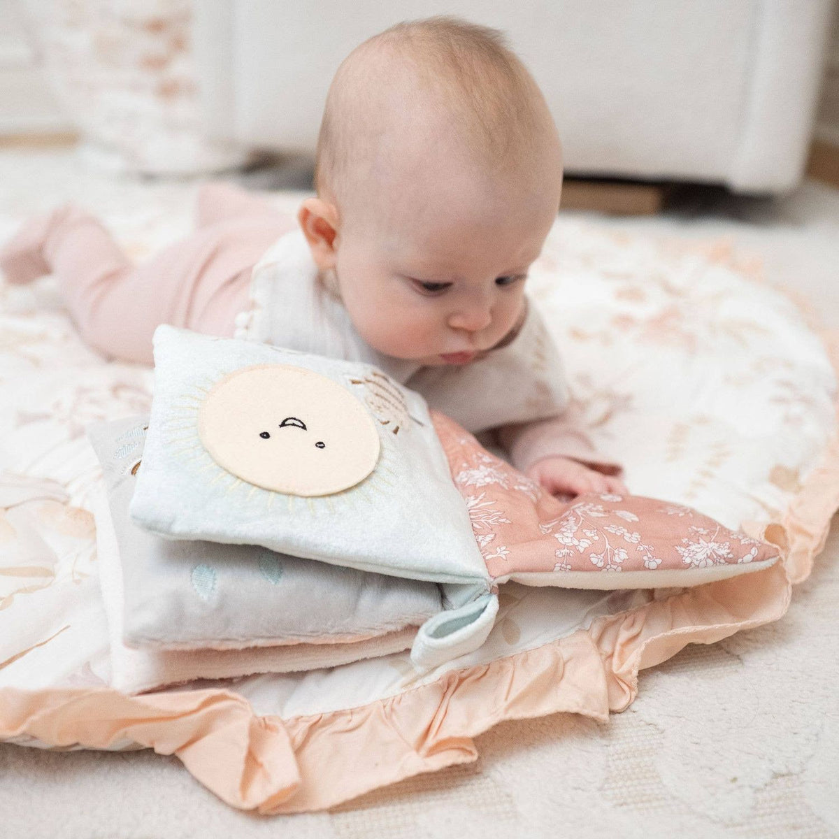small baby laying on a play mat looking at a crinkle book