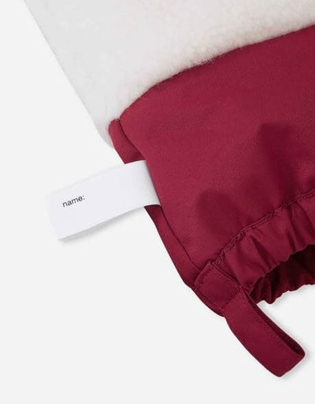 Close-up of a burgundy fabric accessory with a white plush lining and a white fabric tag printed with the name &