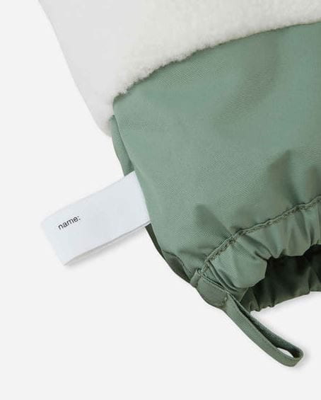 Close-up of a sage green drawstring pouch with a white fleece lining and a white fabric tag printed with the name &