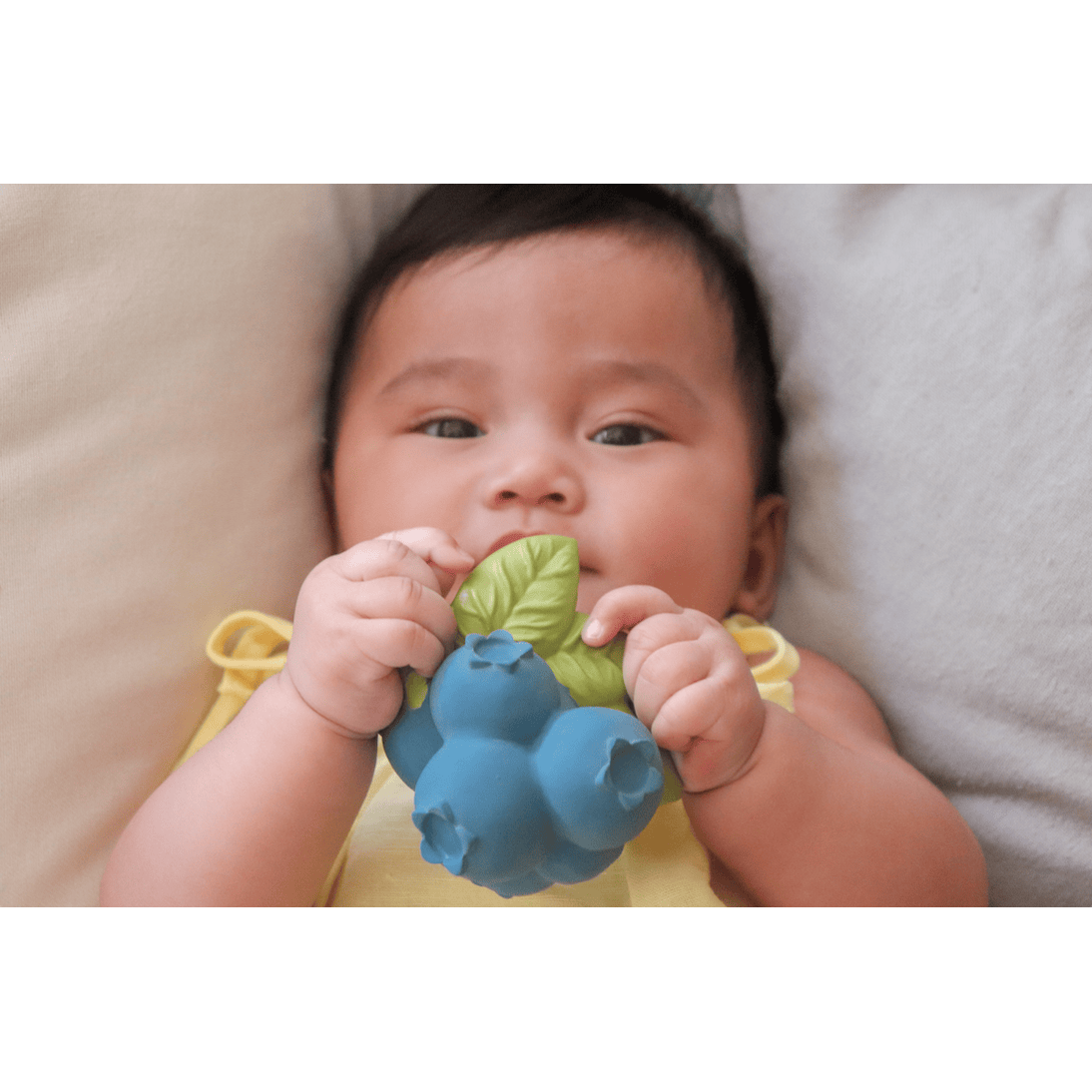 Baby holding a blue teething toy with green leaves